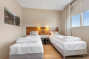 Habitación de hotel con dos camas, cabecero de madera, una mesita pequeña y un ventanal amplio.