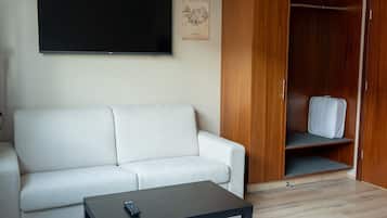 A modern living room with a white sofa, a small black table, a wooden wardrobe, and a flat-screen TV mounted on the wall.