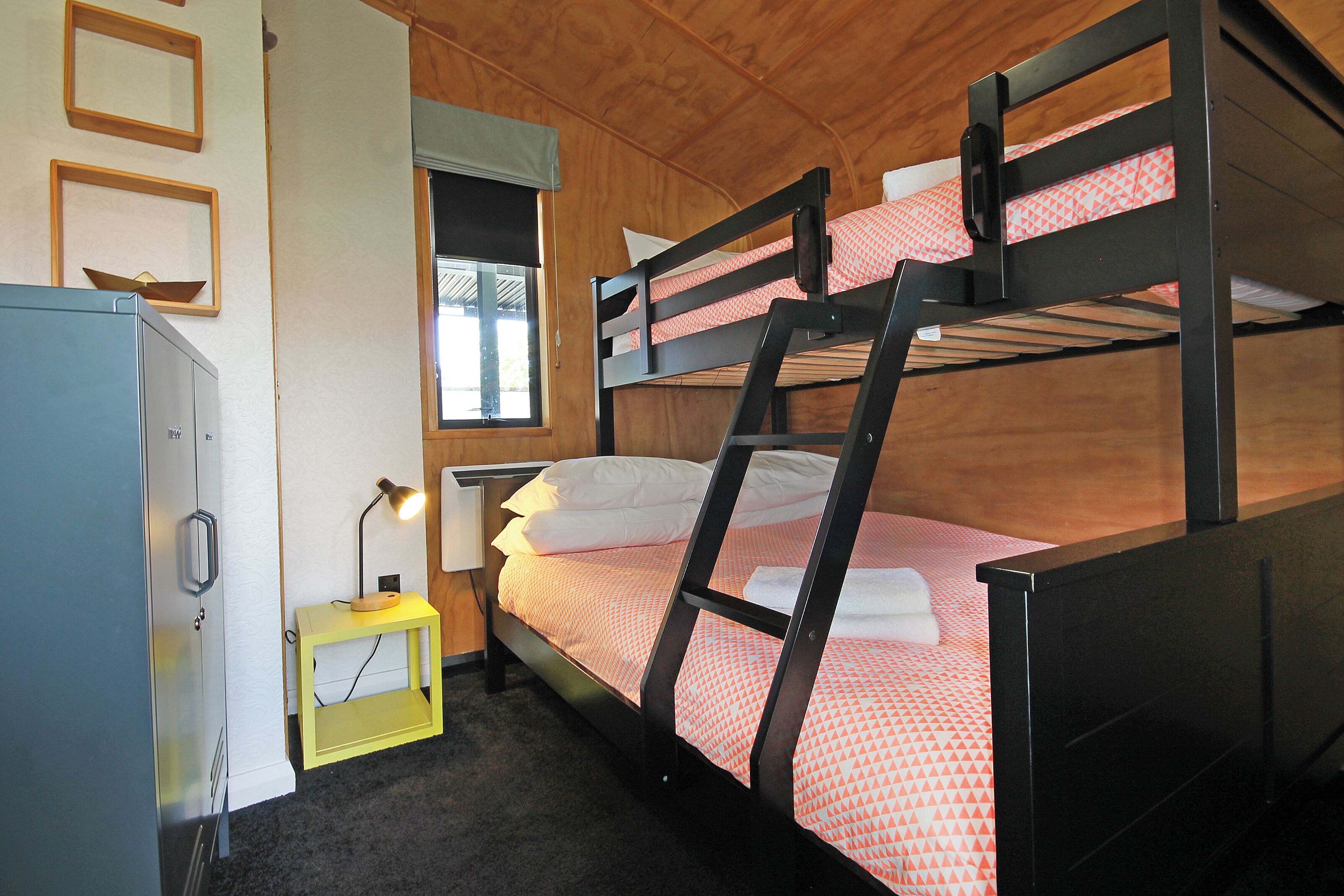 A bunk bed with a wooden headboard, a bedside table with a lamp, and a window with a view.