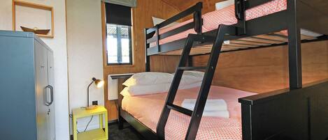 A bunk bed with a wooden headboard, a bedside table with a lamp, and a window with a view.