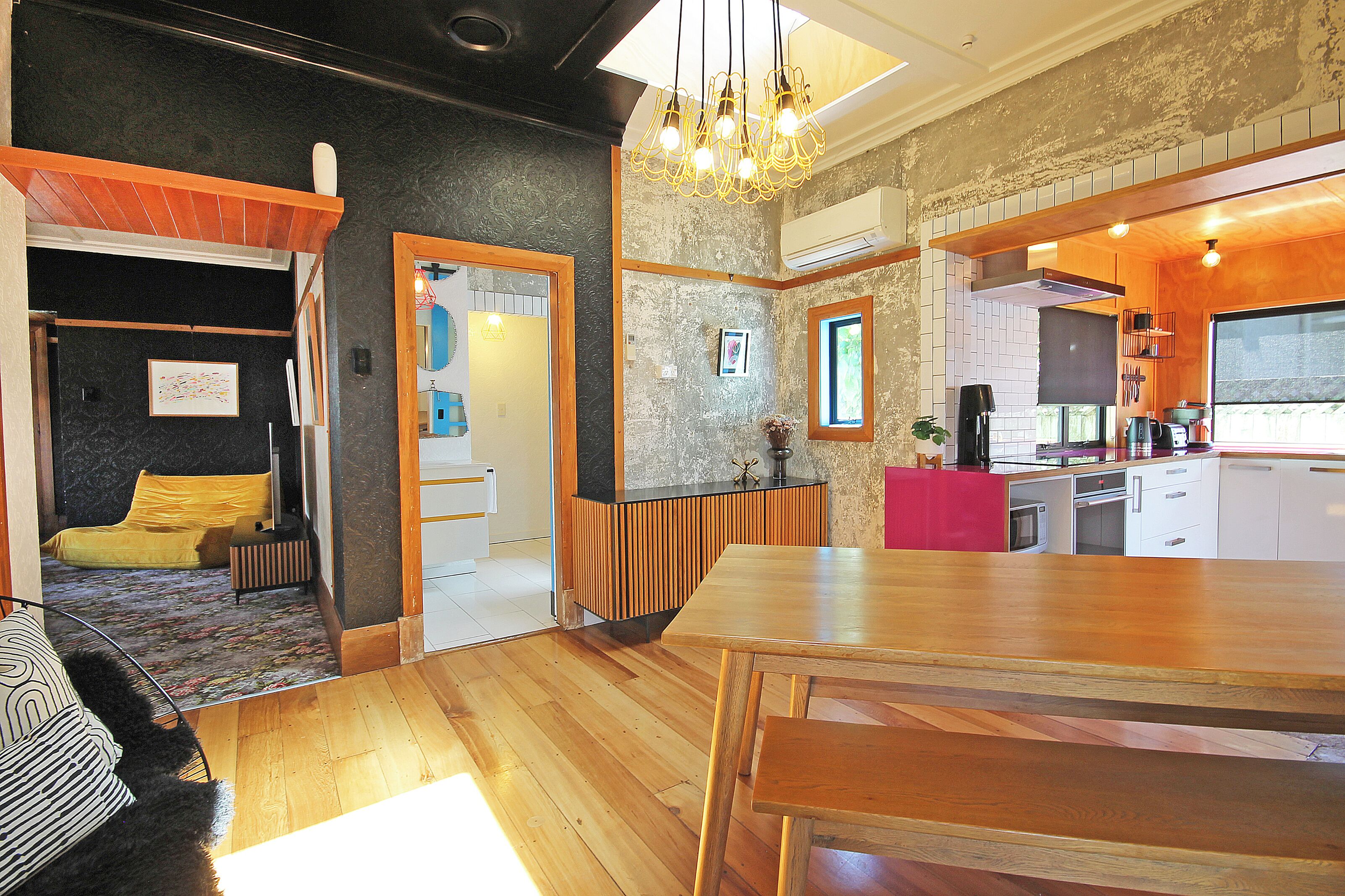 Een moderne keuken met houten aanrecht, een eethoek met een grote houten tafel, en een gezellige zithoek met een bank en een gele deken.