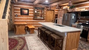 Una cocina de estilo cabaña con una isla central, taburetes de bar de madera, una mesa de comedor y un espejo grande.