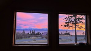 Dos ventanas con vistas a un paisaje que incluye un árbol, un edificio y montañas.