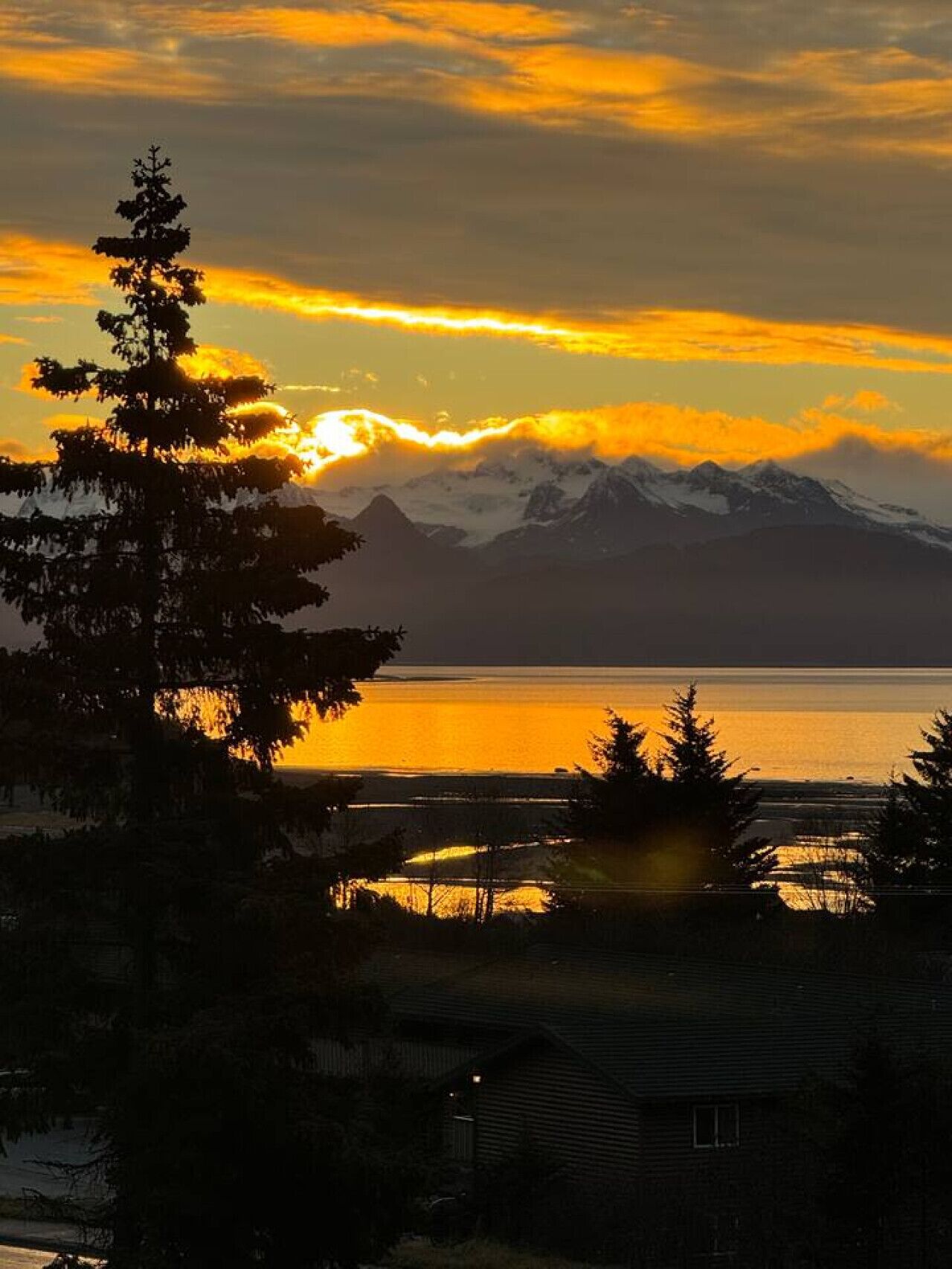 Eine Berglandschaft mit Sonnenuntergang, einem Gewässer und einem Haus im Vordergrund.