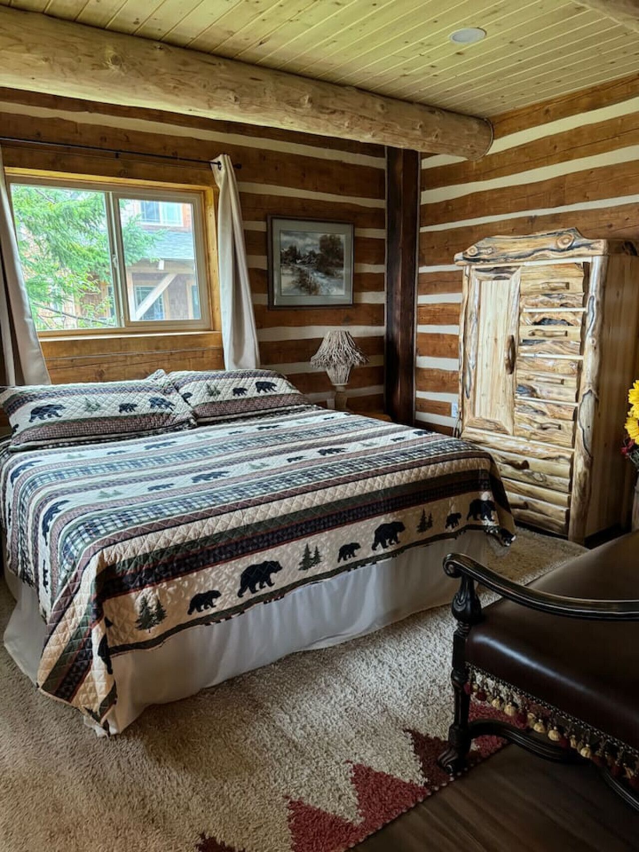 Un dormitorio de cabaña de madera con una cama grande, un armario de madera y una ventana con cortinas.