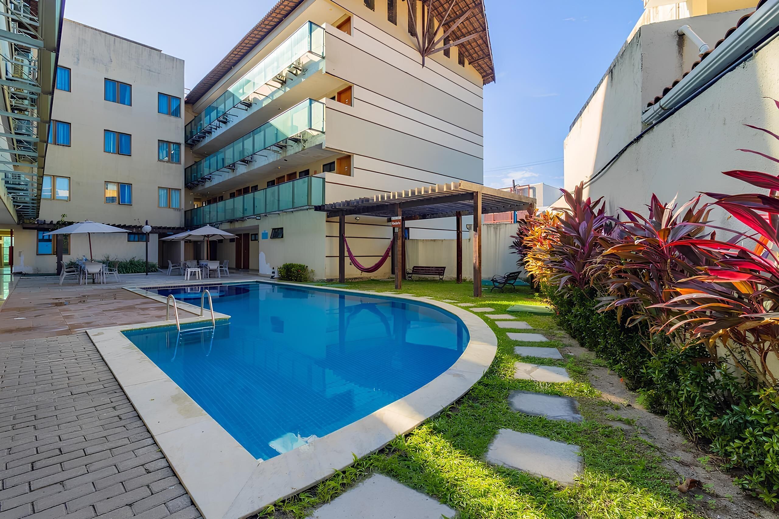 A swimming pool with a surrounding patio area, a covered seating area, and a building with multiple balconies.