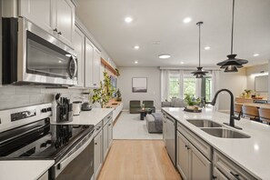 Eine moderne Küche mit Edelstahlgeräten, einer zentralen Kochinsel mit Spüle sowie einem Essbereich mit Sofa und Tisch.