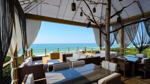 Un'area salotto esterna coperta con tavoli e sedie, con vista sulla spiaggia.