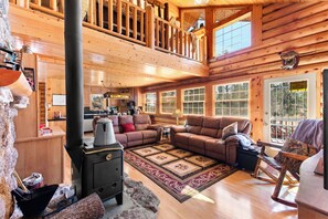 A log cabin interior with a living room, fireplace, and a kitchen area.