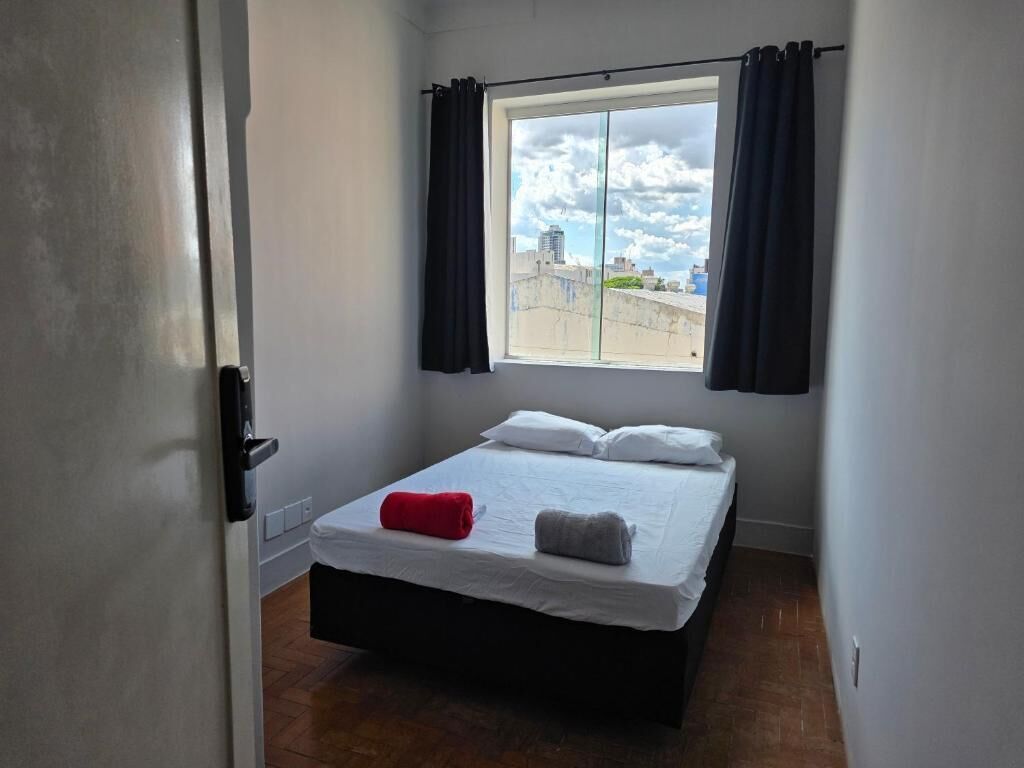 A small, single-bed room with a window and curtains, a door, and a tiled floor.