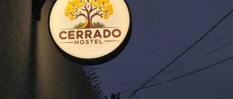 A sign for 'Cerrado Hostel' with a logo featuring a tree and yellow flowers.