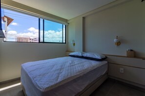Ein Schlafzimmer mit einem Bett, einem Fenster, einer Wandleuchte und einem Regal mit einem Korb.