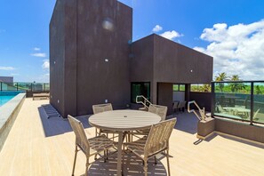Eine Dachterrasse mit rundem Tisch und Korbstühlen mit Blick auf einen Swimmingpool und Palmen.
