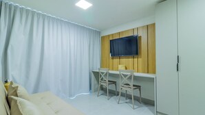 A room with a sofa, two chairs, a TV mounted on a wooden panel wall, and a wardrobe. - Ocean Blue #01 - Apt With Pool by Carpediem (Ipojuca)