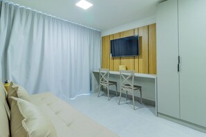 A room with a sofa, two chairs, a TV mounted on a wooden panel wall, and a wardrobe. - Ocean Blue #01 - Apt With Pool by Carpediem (Ipojuca)