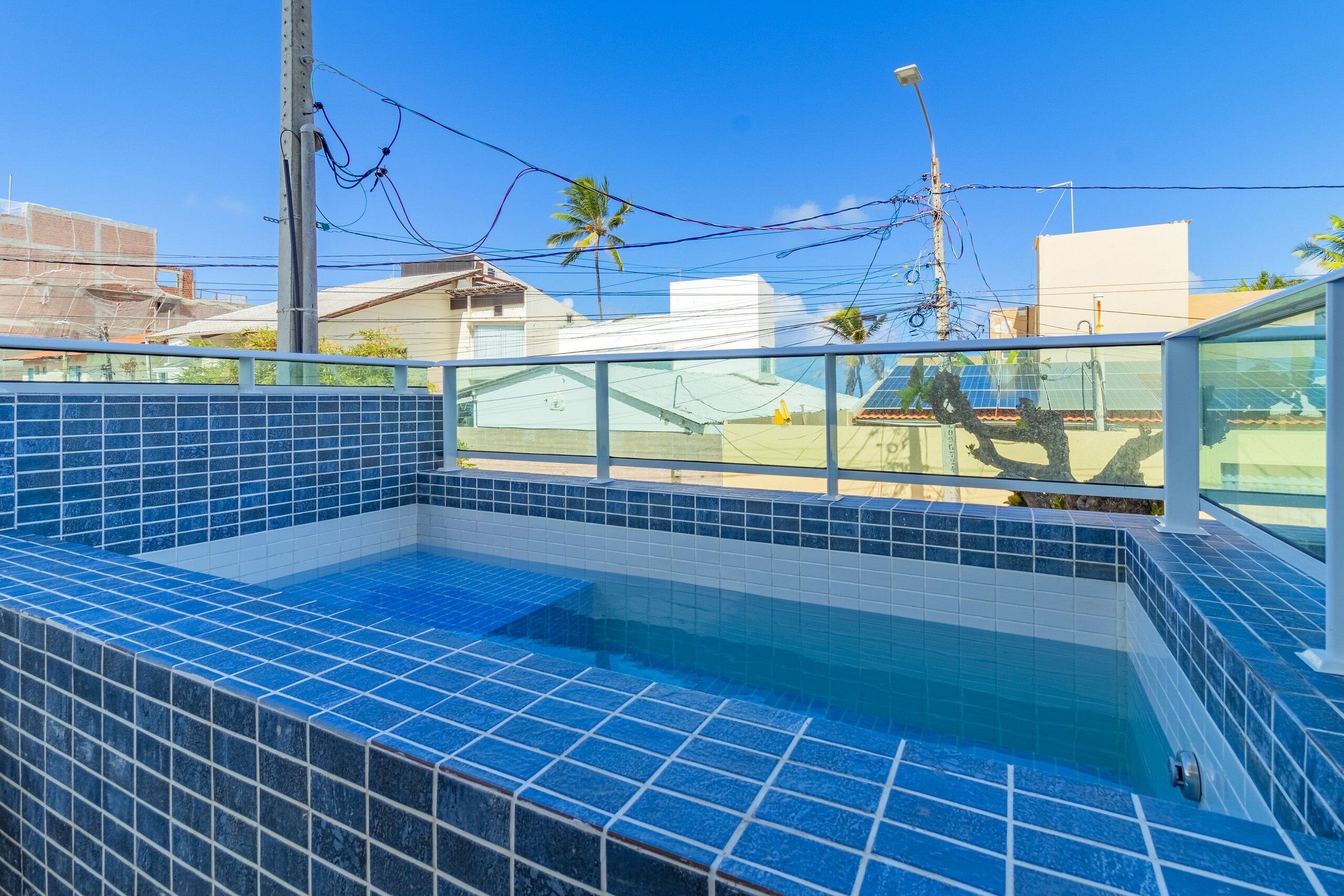 A rooftop swimming pool with blue tiles and a glass railing.