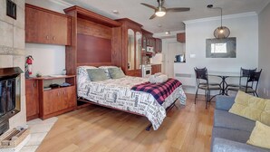 Ein Schlafzimmer mit einem Bett, Holzschränken, einem Kamin, einem Deckenventilator und einem Essbereich mit Stühlen.