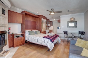A bedroom with a bed, wooden cabinets, a fireplace, a ceiling fan, and a dining area with chairs. - Au p'tit cocon sur le lac (Magog)