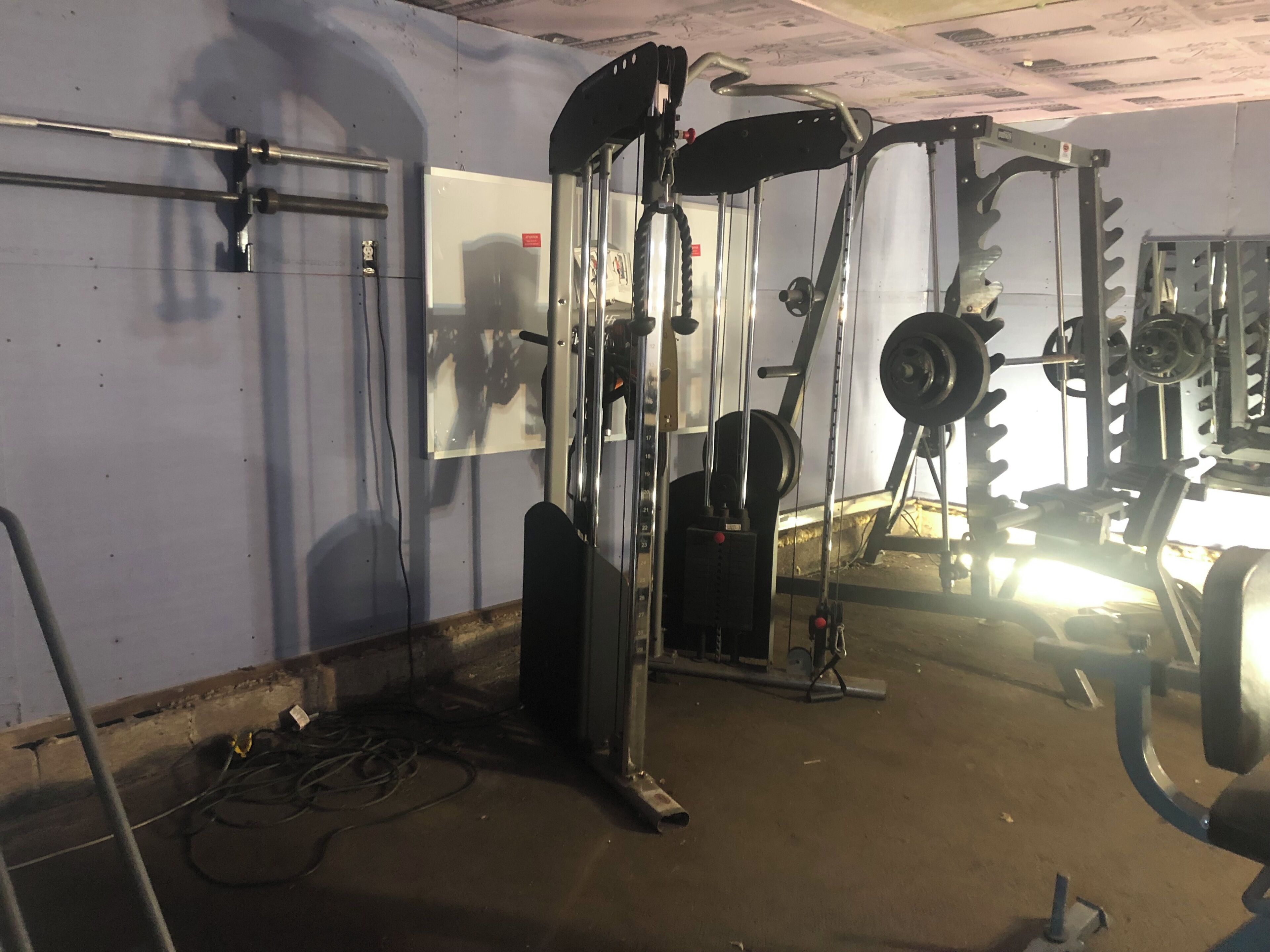 Un gimnasio con equipo de levantamiento de pesas, espejos y suelo de hormigón.