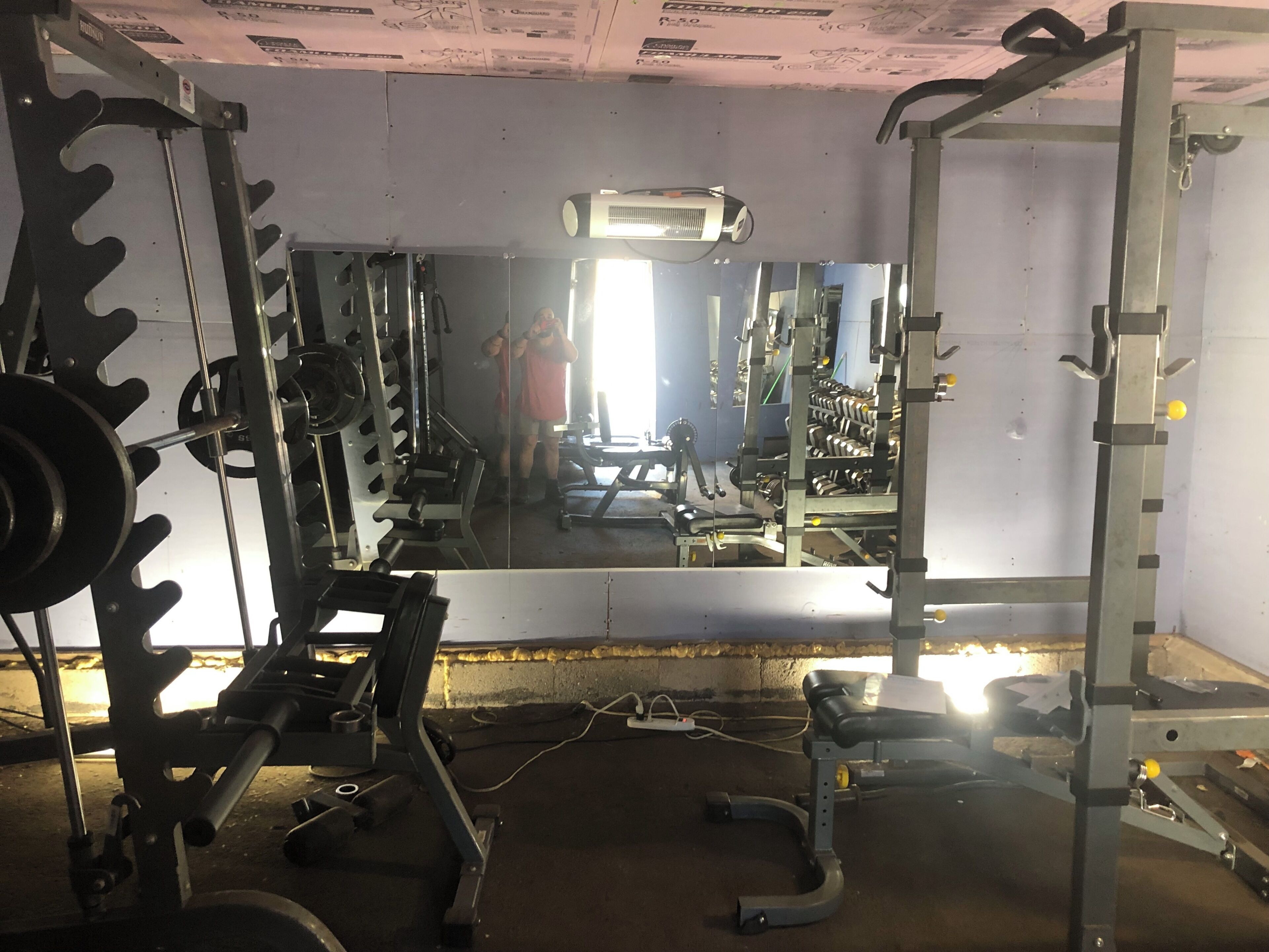 A gym with weightlifting equipment, a large mirror, and a ceiling fan.