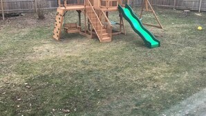 Une structure de jeu en bois avec un toboggan, installée dans un jardin.