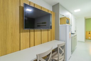 Eine moderne Küche mit integriertem Mikrowellenofen, einem weißen Esstisch und einem an einer Holzwand montierten Fernseher.