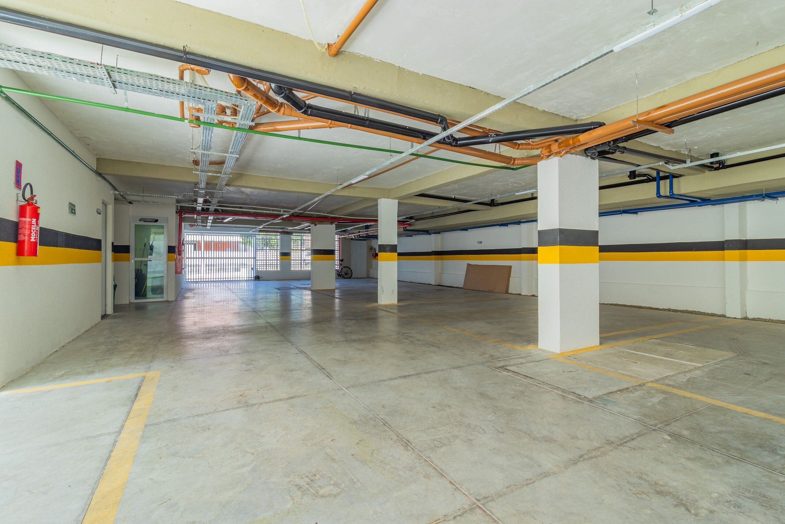 An indoor parking garage with concrete floors, yellow and black striped walls, and visible fire extinguishers.