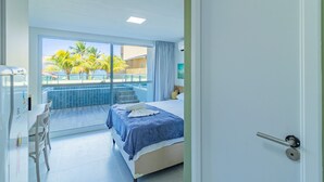 Habitación de hotel con cama, zona de comedor y vista a una piscina y palmeras.