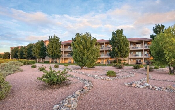 Un hôtel à plusieurs étages doté d’une cour aménagée avec un chemin de gravier, des arbres et des arbustes.