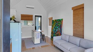 Un salon moderne avec un canapé gris clair, un coin cuisine doté d’un réfrigérateur bleu et une peinture abstraite aux couleurs vives accrochée au mur.