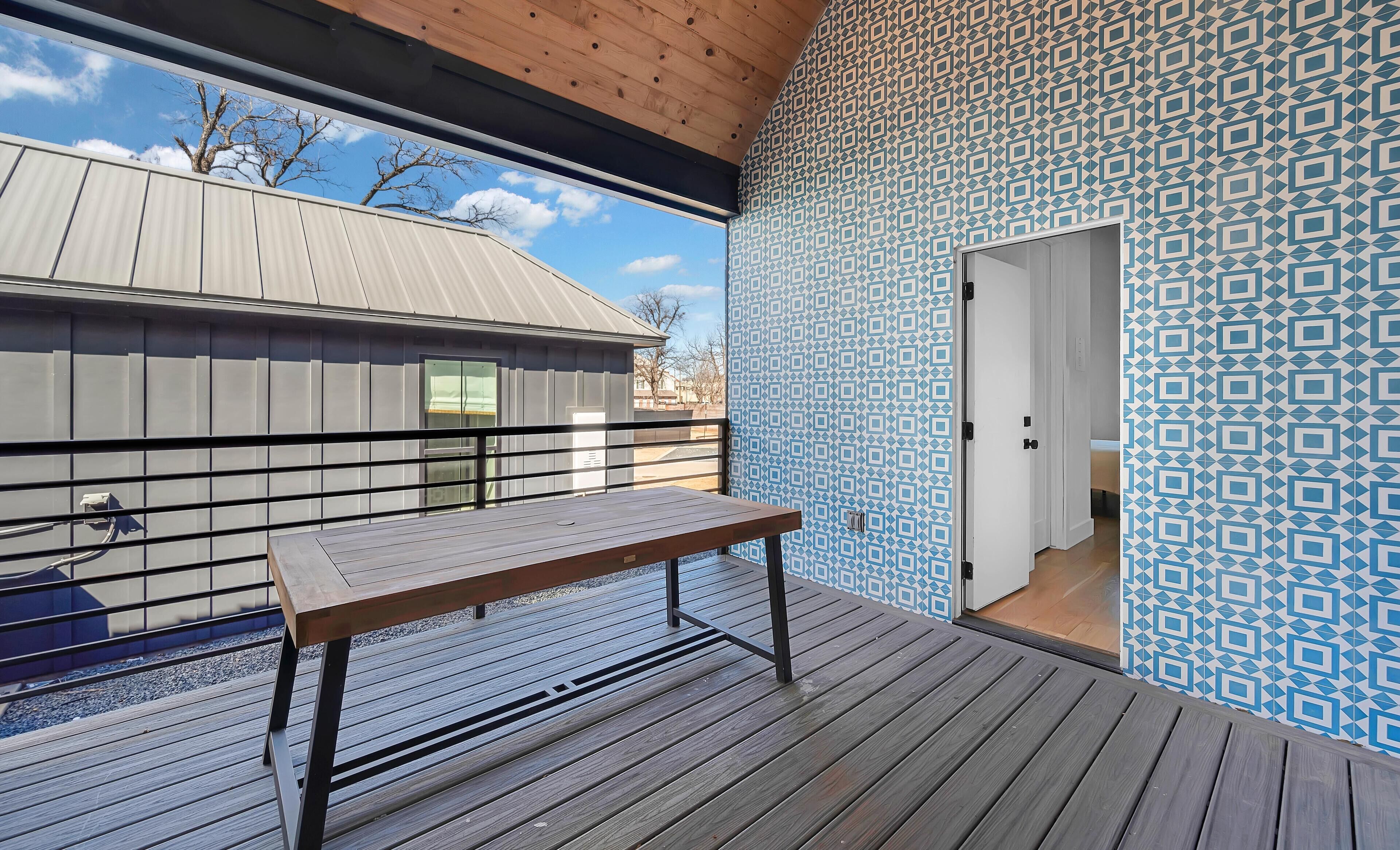 A wooden deck with a bench, a patterned wall, and a door leading to an interior room.