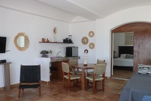 Une pièce comprenant une table à manger, des chaises, un téléviseur, un coin cuisine et un lit.
