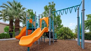 A playground with two orange slides, a climbing structure, and a swing set. - WorldMark St. George - 2 Bedroom Deluxe (St. George)