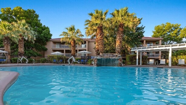 A swimming pool with palm trees and a waterfall feature, surrounded by lounge chairs and umbrellas. - WorldMark St. George - 2 Bedroom Twin (St. George)