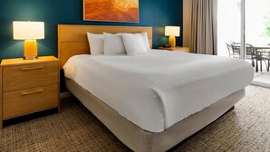 A hotel room with a large bed, wooden headboard, two bedside tables with lamps, a large window with curtains, and a painting on the wall. - WorldMark St. George - 2 Bedroom Twin (St. George)