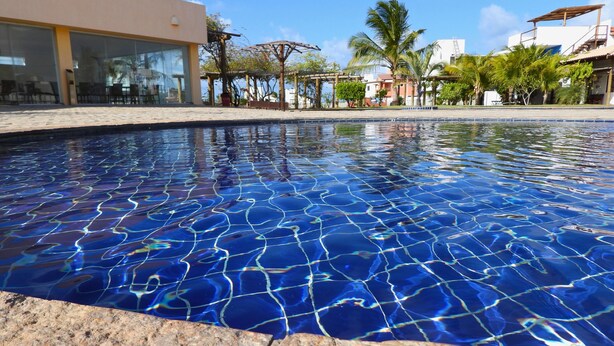 Una piscina con superficie de agua cristalina y azul, rodeada por un edificio moderno con grandes ventanales y un área de patio.