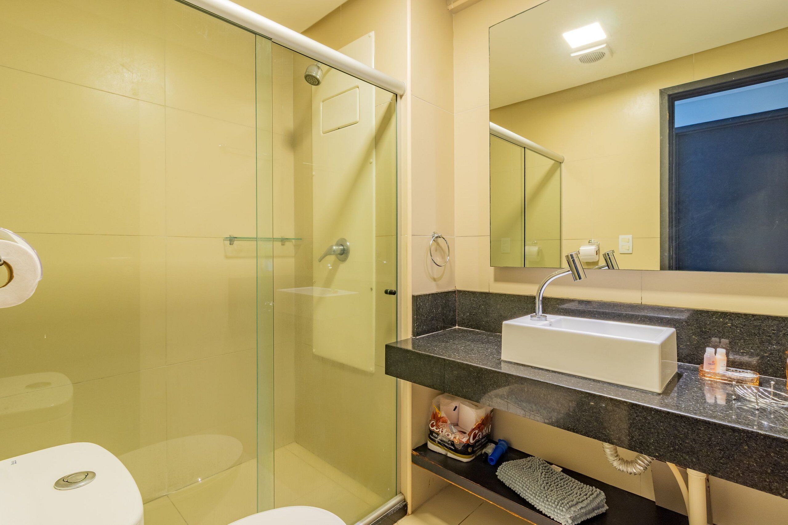 Un baño con ducha envuelta en vidrio, un lavabo blanco y un espejo sobre el lavabo.