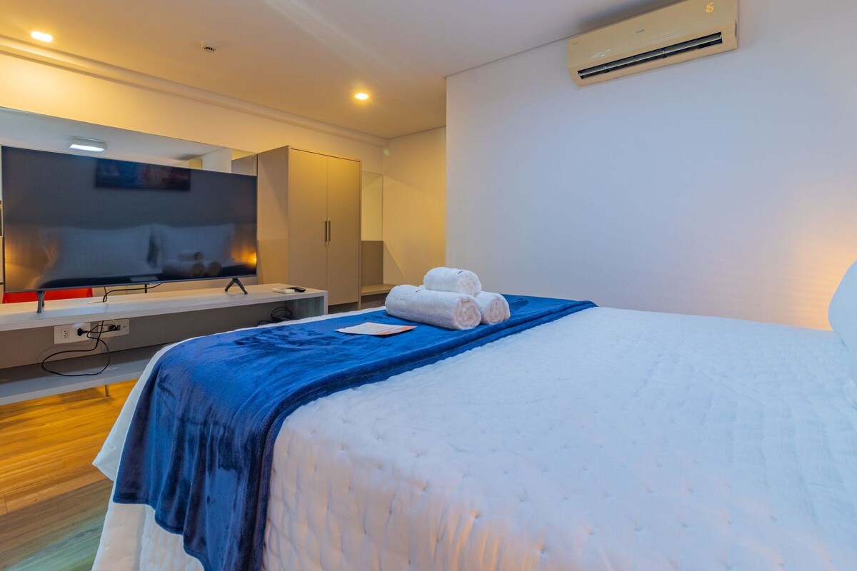 A modern hotel room with a large bed, a flat-screen TV, a wardrobe, and an air conditioning unit.