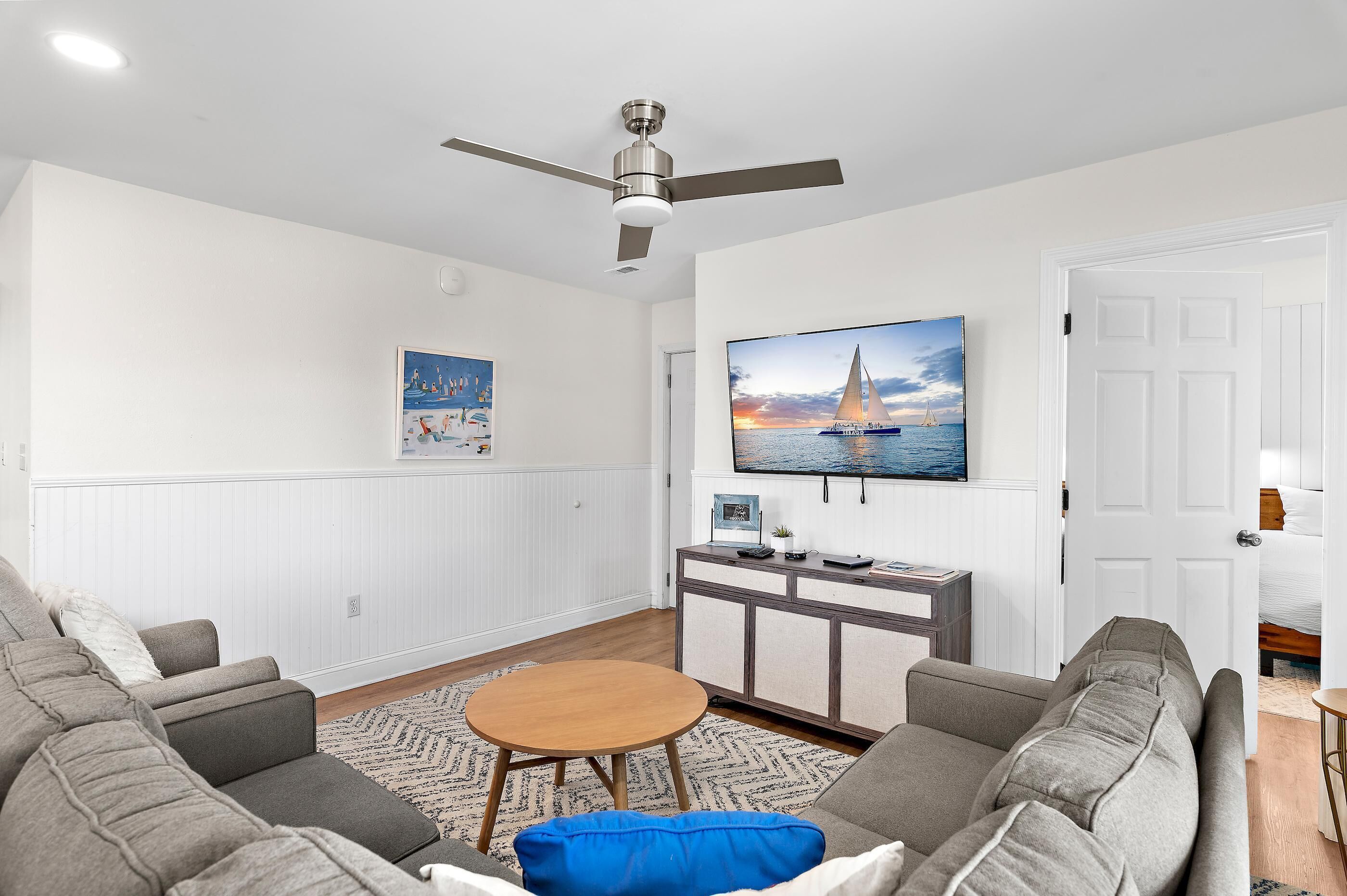 A living room with a ceiling fan, a TV mounted on the wall, a sofa, a coffee table, and a cabinet.