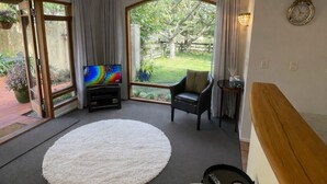Ett modernt vardagsrum med en stor, rund matta, en soffa, en tv och utsikt över en trädgård genom en glasdörr.