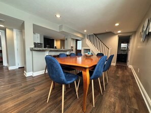 A dining area with a wooden table and blue chairs, a kitchen in the background, and a staircase leading to another level. - 2BR Winona Lake Garden Suite | Walk to Village |   Dog Friendly | Near Grace (Winona Lake)