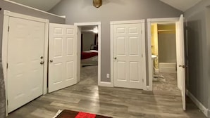 A spacious room with a sloped ceiling, wooden flooring, and white doors. - Buckeye Cottage (Willard)