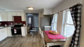 A modern kitchen with white cabinets, a stainless steel refrigerator, and a wooden dining table with chairs. - Buckeye Cottage (Willard)