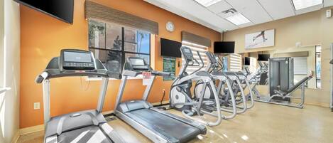 Un gimnasio con cintas de correr, elípticas y una banca para pesas.