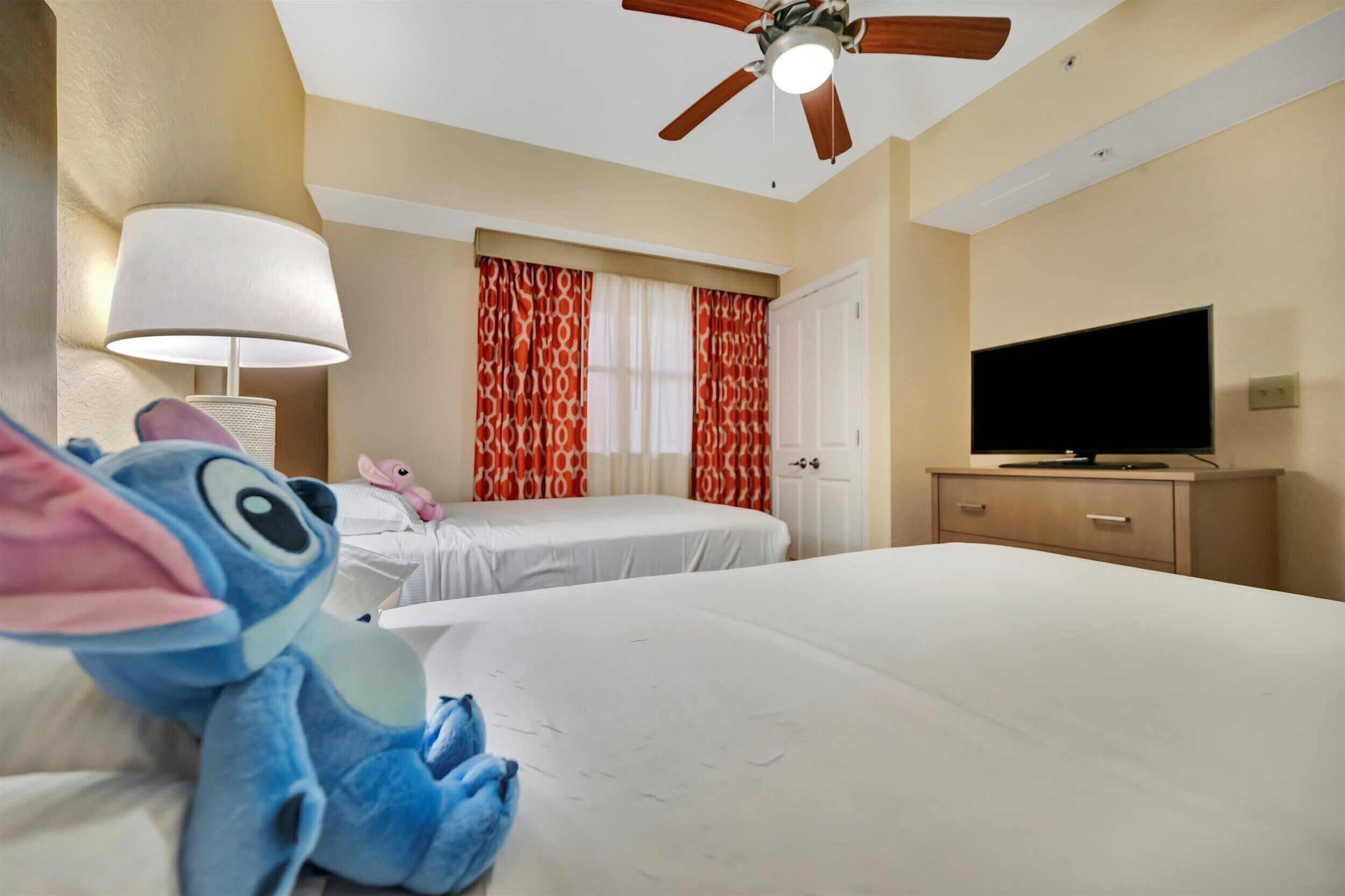 Une chambre d’hôtel avec deux lits, un ventilateur de plafond, une télévision et une lampe.