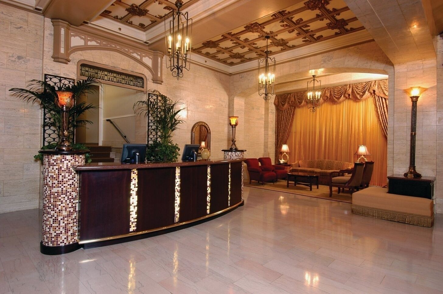 A lobby with a reception desk, seating area, and decorative elements like plants and chandeliers.