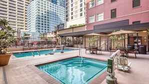 A rooftop pool area with lounge chairs and umbrellas, surrounded by high-rise buildings.