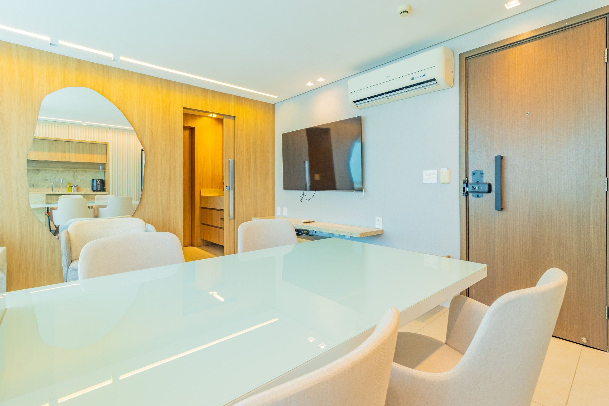 A modern conference room with a glass table, white chairs, a mounted TV, and an air conditioning unit.