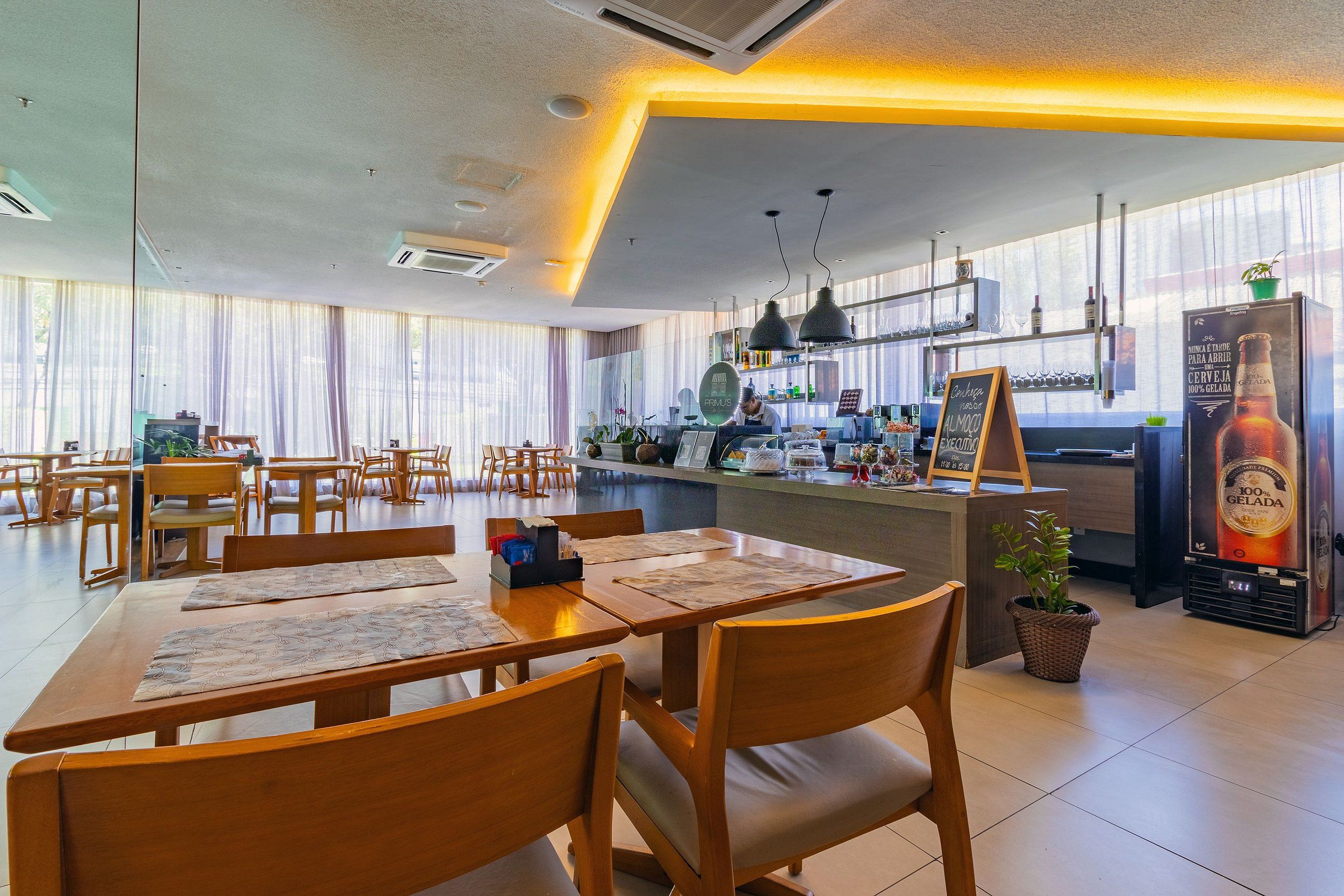 A restaurant with wooden tables and chairs, a bar area with a counter, and a large window with curtains.
