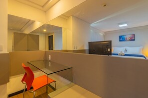 A modern hotel room with a glass partition, a single bed, a television, and a red chair. - Homes Stay #2306 - Ideal Location in Carpediem (Recife)